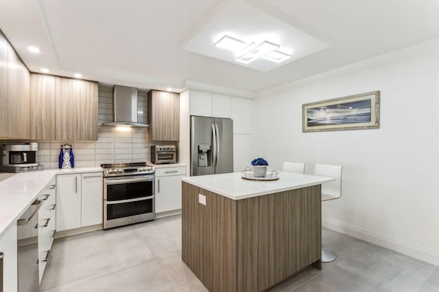 kitchen with white cabinets, wall chimney range hood, appliances with stainless steel finishes, and tasteful backsplash