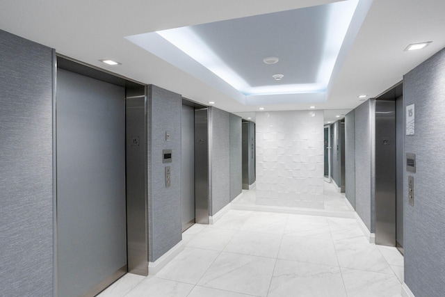 hallway with elevator and a tray ceiling