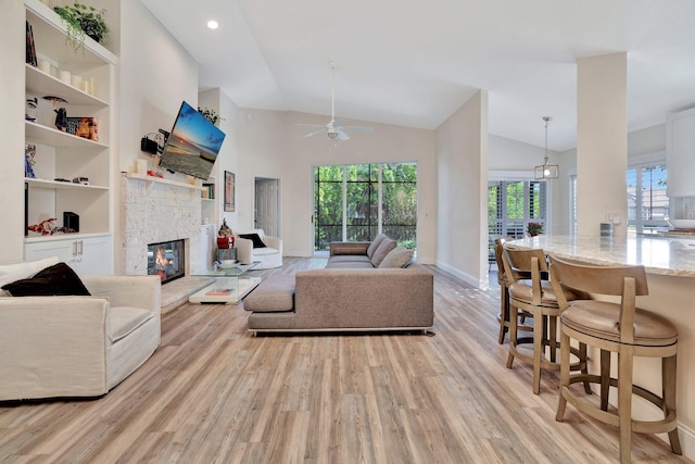 living room featuring built in shelves, ceiling fan, light hardwood / wood-style flooring, high vaulted ceiling, and a fireplace