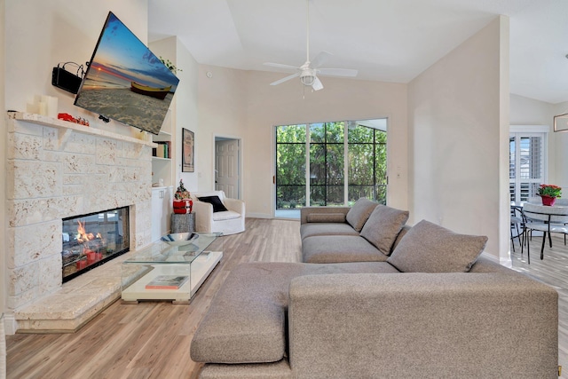 living room with a fireplace, light wood-type flooring, vaulted ceiling, and ceiling fan