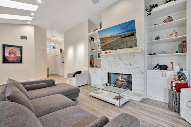 living room with lofted ceiling with skylight, built in features, and light hardwood / wood-style floors