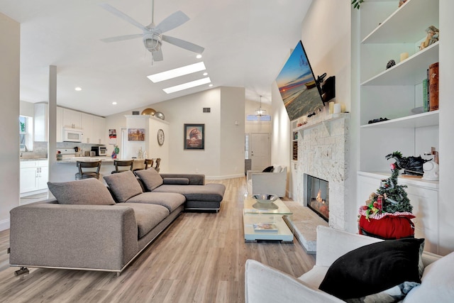 living room featuring a fireplace, ceiling fan, light hardwood / wood-style flooring, and vaulted ceiling