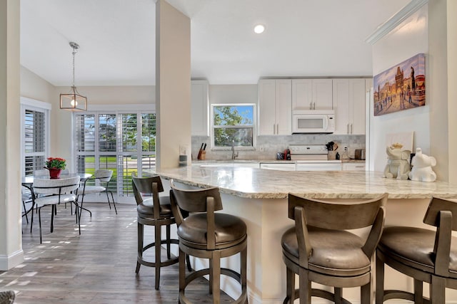 kitchen with white cabinetry, hanging light fixtures, dark hardwood / wood-style flooring, kitchen peninsula, and white appliances