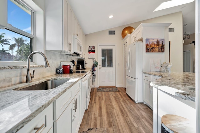 kitchen featuring light stone countertops, light wood-type flooring, white appliances, lofted ceiling with skylight, and white cabinets