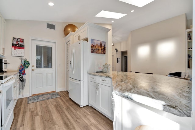 kitchen featuring light wood-type flooring, light stone counters, vaulted ceiling with skylight, white appliances, and white cabinets