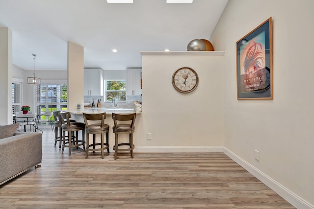 interior space with white cabinets, hanging light fixtures, light hardwood / wood-style floors, a kitchen bar, and kitchen peninsula