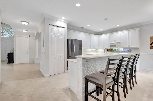 kitchen with white cabinets, stainless steel fridge, crown molding, and a breakfast bar area