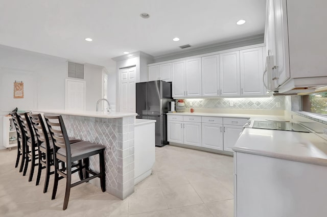 kitchen featuring stainless steel fridge, white cabinetry, a breakfast bar, and a kitchen island