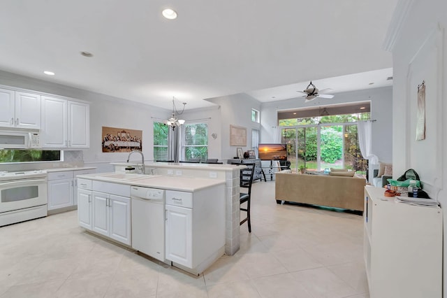 kitchen with sink, white appliances, a kitchen island with sink, white cabinets, and ceiling fan with notable chandelier