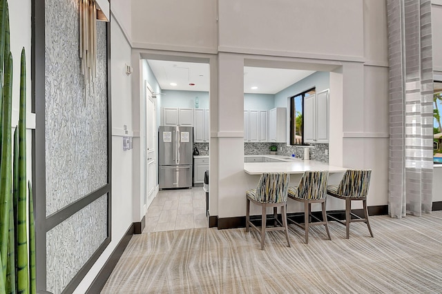 kitchen featuring white cabinets, a kitchen breakfast bar, stainless steel fridge, tasteful backsplash, and kitchen peninsula