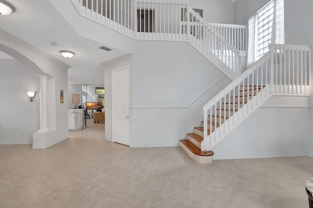 staircase featuring ornamental molding, a high ceiling, and decorative columns