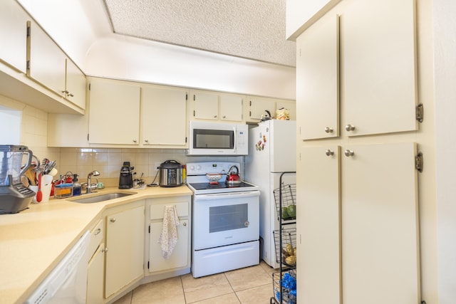 kitchen featuring sink, backsplash, white appliances, cream cabinetry, and light tile patterned flooring