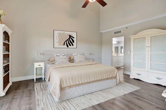 bedroom with ceiling fan, connected bathroom, a towering ceiling, and hardwood / wood-style flooring