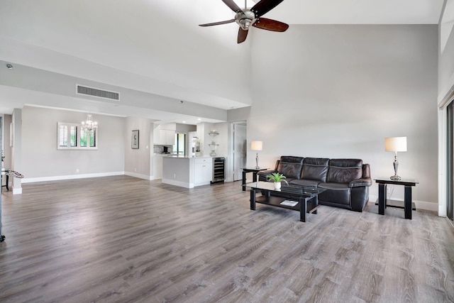 living room with ceiling fan with notable chandelier, a towering ceiling, light hardwood / wood-style floors, and wine cooler