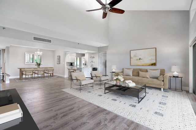 living room featuring ceiling fan with notable chandelier, wood-type flooring, and a high ceiling