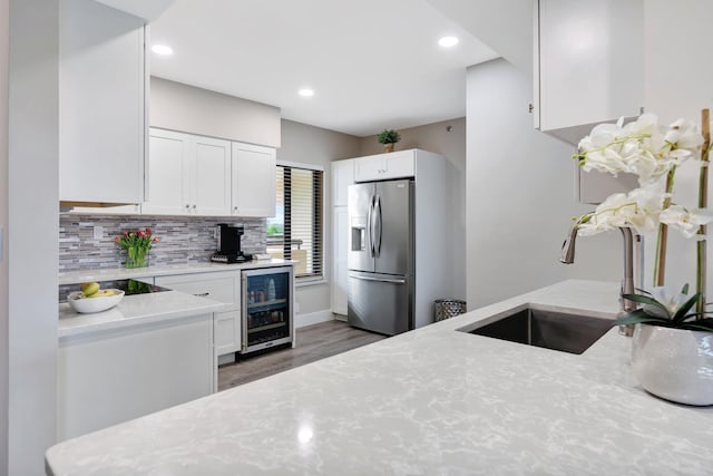 kitchen with light stone counters, stainless steel fridge with ice dispenser, wine cooler, white cabinetry, and sink