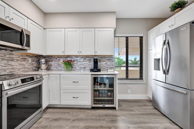 kitchen with stainless steel appliances, white cabinets, light wood-type flooring, backsplash, and wine cooler