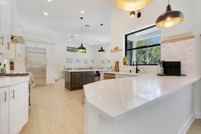 kitchen featuring white cabinetry, hanging light fixtures, high end appliances, and kitchen peninsula