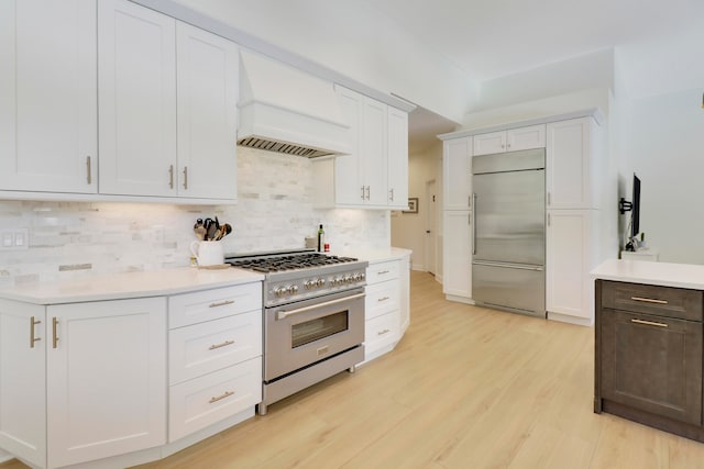 kitchen with high quality appliances, custom range hood, white cabinets, and backsplash