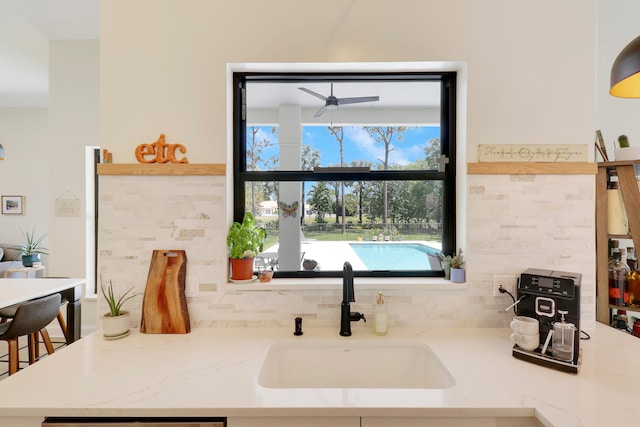 kitchen featuring light stone counters, sink, decorative backsplash, and ceiling fan