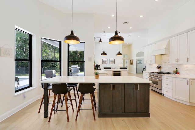 kitchen with pendant lighting, high end stove, white cabinets, custom range hood, and a spacious island