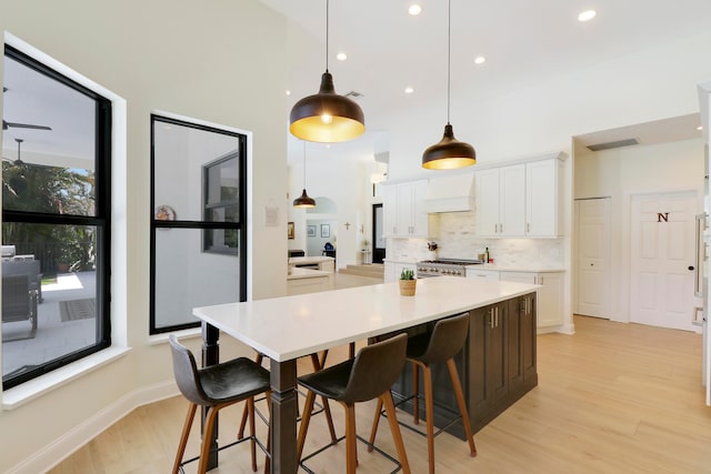 kitchen with light hardwood / wood-style flooring, stainless steel range oven, hanging light fixtures, and white cabinets