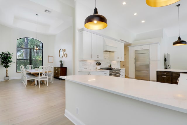 kitchen with premium range hood, high quality appliances, white cabinetry, hanging light fixtures, and a tray ceiling