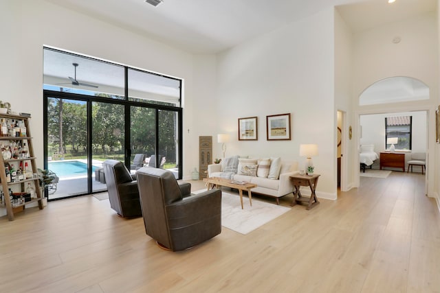 living room featuring ceiling fan, a towering ceiling, and light wood-type flooring