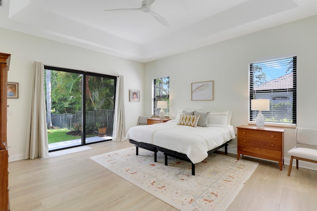 bedroom with light hardwood / wood-style floors, access to exterior, ceiling fan, and a tray ceiling