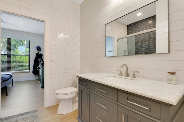 bathroom featuring hardwood / wood-style flooring, tile walls, vanity, toilet, and walk in shower