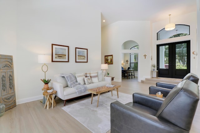 living room featuring high vaulted ceiling, light hardwood / wood-style floors, and french doors