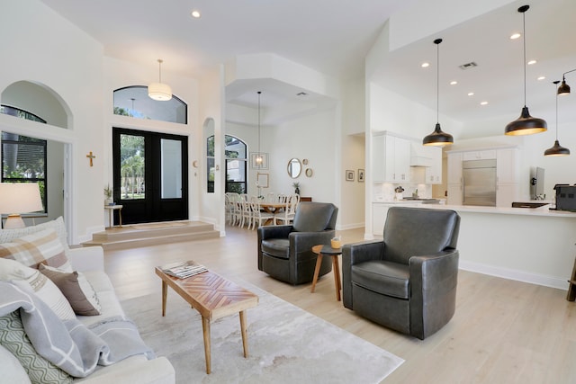 living room with french doors, a towering ceiling, and light hardwood / wood-style flooring