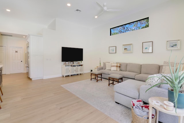 living room with a high ceiling, ceiling fan, and light hardwood / wood-style floors