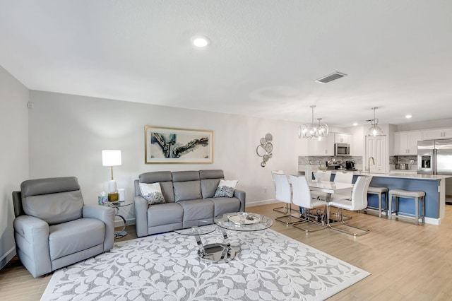 living room featuring sink, light hardwood / wood-style floors, and an inviting chandelier