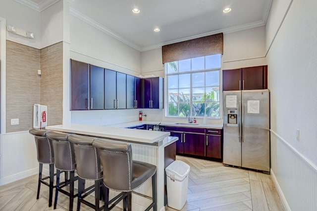 kitchen with kitchen peninsula, stainless steel refrigerator with ice dispenser, a breakfast bar, crown molding, and sink