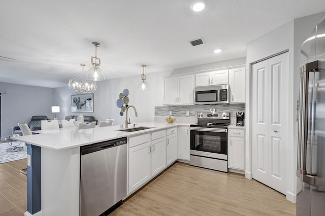 kitchen featuring sink, kitchen peninsula, light hardwood / wood-style floors, decorative light fixtures, and appliances with stainless steel finishes