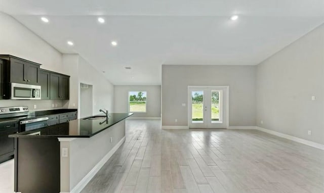 kitchen featuring appliances with stainless steel finishes, dark stone counters, sink, a center island with sink, and light hardwood / wood-style floors