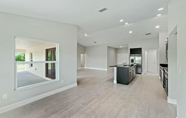 kitchen with stainless steel fridge, sink, an island with sink, and light hardwood / wood-style floors