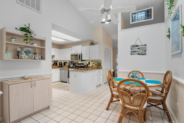 kitchen featuring white cabinetry, stainless steel appliances, high vaulted ceiling, dark stone counters, and light tile patterned floors