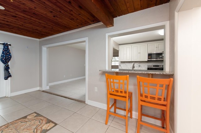 kitchen with light tile patterned floors, backsplash, stainless steel appliances, white cabinets, and wooden ceiling