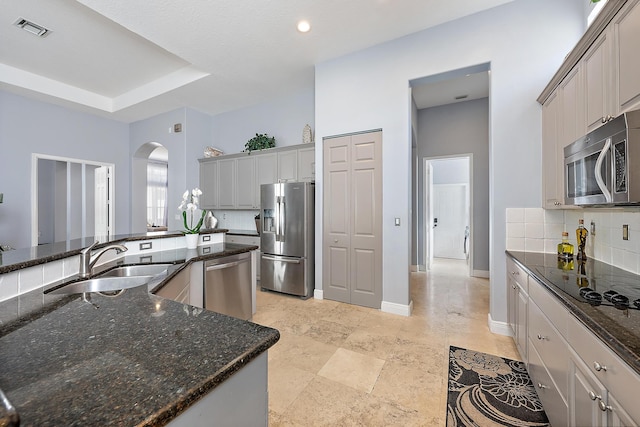 kitchen featuring backsplash, dark stone counters, gray cabinetry, stainless steel appliances, and sink