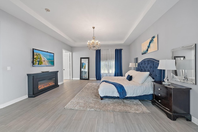 bedroom featuring a notable chandelier, a raised ceiling, and light hardwood / wood-style flooring