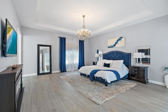 bedroom featuring a tray ceiling, light hardwood / wood-style floors, and a notable chandelier