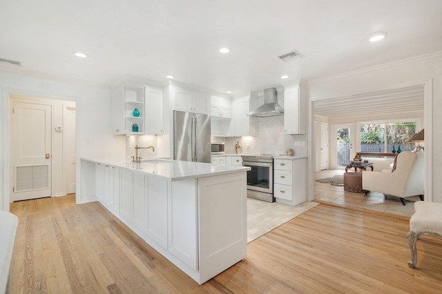 kitchen featuring wall chimney range hood, appliances with stainless steel finishes, light hardwood / wood-style floors, white cabinets, and ornamental molding