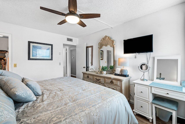 bedroom with a textured ceiling, ceiling fan, and dark wood-type flooring