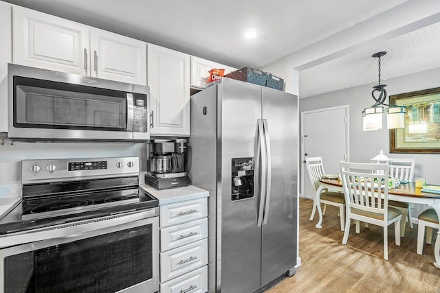 kitchen featuring pendant lighting, light wood-type flooring, a textured ceiling, white cabinetry, and stainless steel appliances