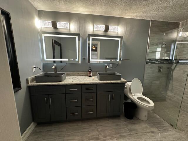 bathroom featuring toilet, vanity, a textured ceiling, and walk in shower