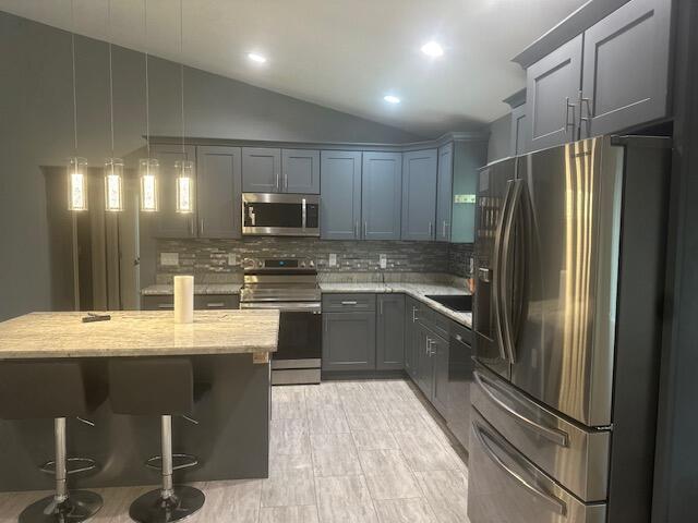 kitchen with decorative backsplash, appliances with stainless steel finishes, light stone counters, a breakfast bar, and hanging light fixtures