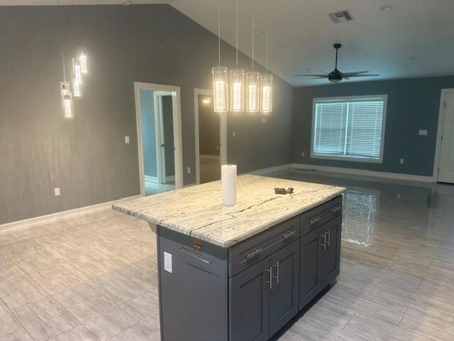 kitchen featuring a center island, lofted ceiling, ceiling fan, decorative light fixtures, and light stone counters