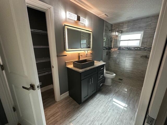 bathroom with a tile shower, vanity, a textured ceiling, and toilet